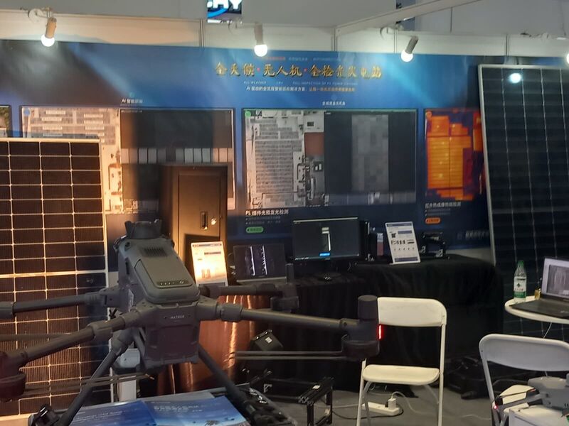 An exhibition booth with an industrial multirotor inspection drone in front of screens showing photoluminescence and infrared-thermal imaging of PV modules.