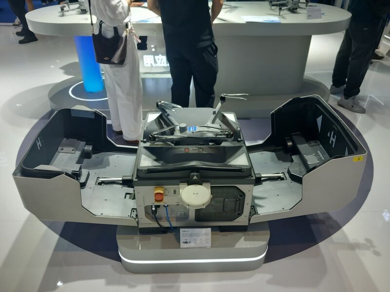 An open box-style landing station with twin H-marked pads and a deployed drone.